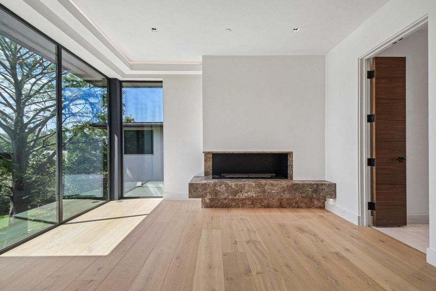 Floor-to-ceiling glass doors flood this modern room with natural light alongside a marble fireplace. Floor-to-ceiling glass doors flood this modern room with natural light alongside a marble fireplace.