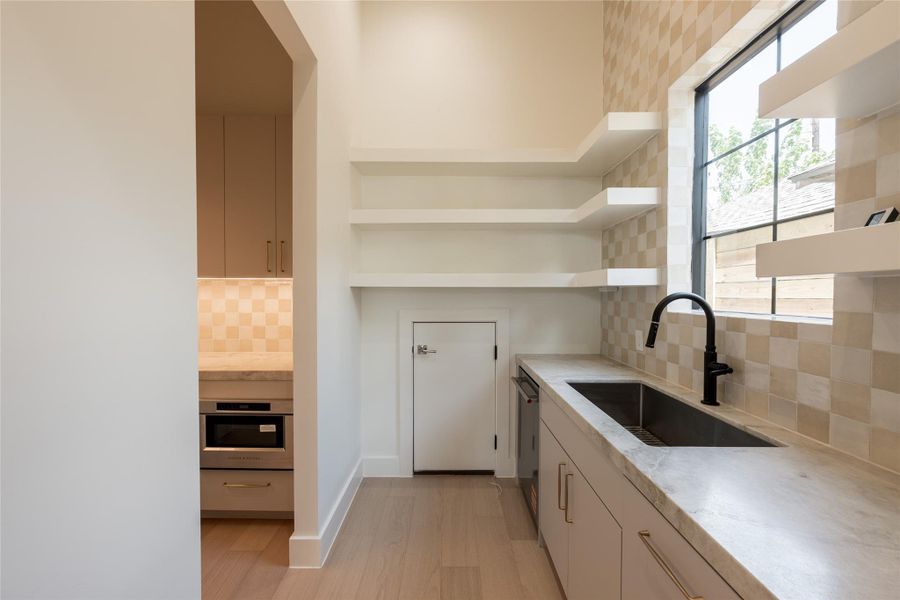 The scullery is designed for more than extra prep and storage, with a dedicated grocery pass through connecting directly from the garage for effortless unloading. Open shelving, natural stone counters and a secondary sink keep everyday function beautifully out of sight. The scullery is designed for more than extra prep and storage, with a dedicated grocery pass through connecting directly from the garage for effortless unloading. Open shelving, natural stone counters and a secondary sink keep everyday function beautifully out of sight.