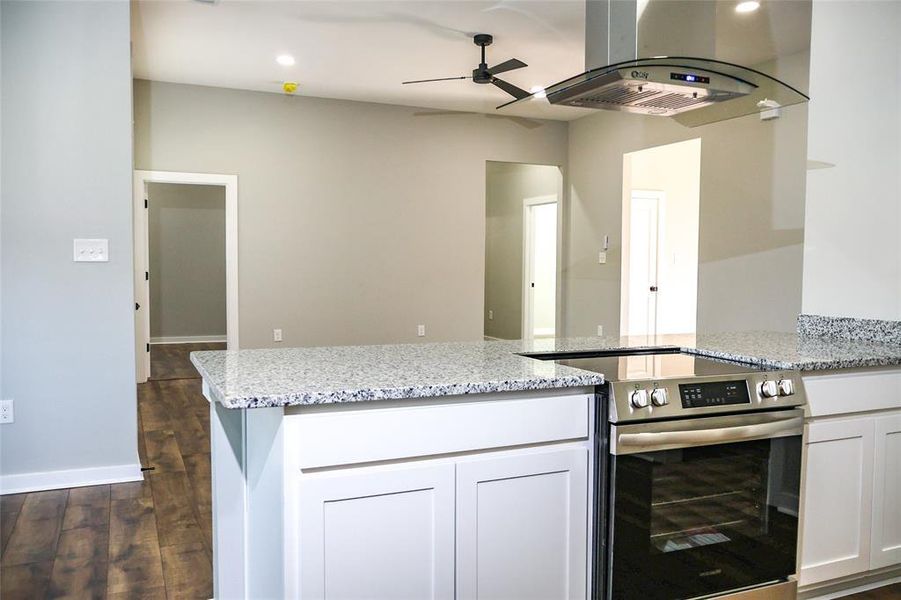 Kitchen featuring electric stove, island range hood, a peninsula, light stone counters, and white cabinetry Kitchen featuring electric stove, island range hood, a peninsula, light stone counters, and white cabinetry