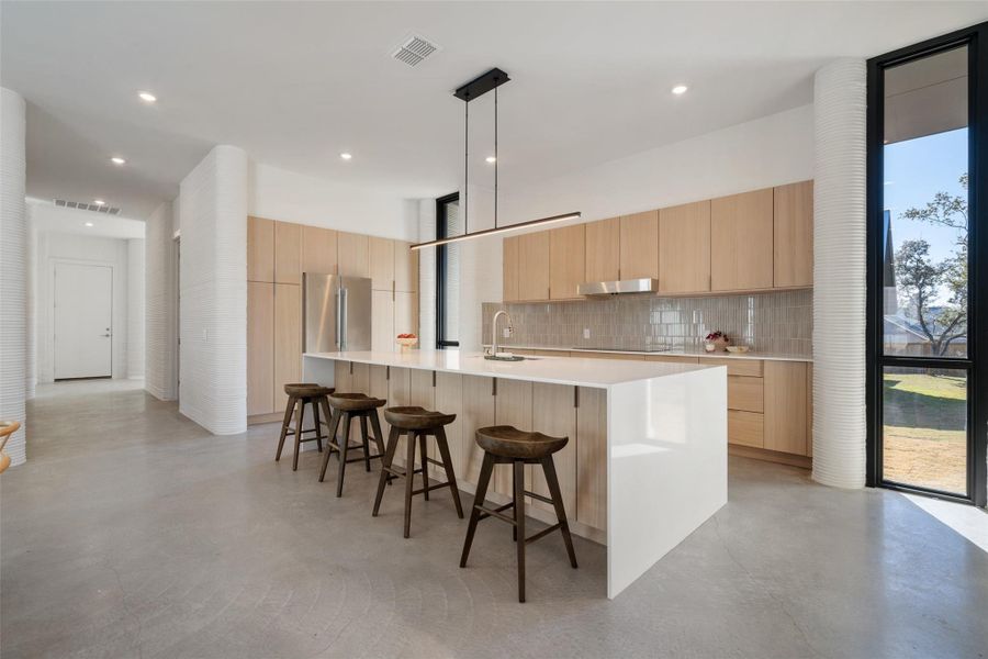 Kitchen featuring decorative light fixtures, sink, high quality fridge, a kitchen breakfast bar, and light brown cabinets