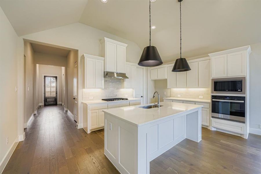 Kitchen with stainless steel appliances, decorative backsplash, vaulted ceiling, white cabinetry, and dark wood finished floors Kitchen with stainless steel appliances, decorative backsplash, vaulted ceiling, white cabinetry, and dark wood finished floors