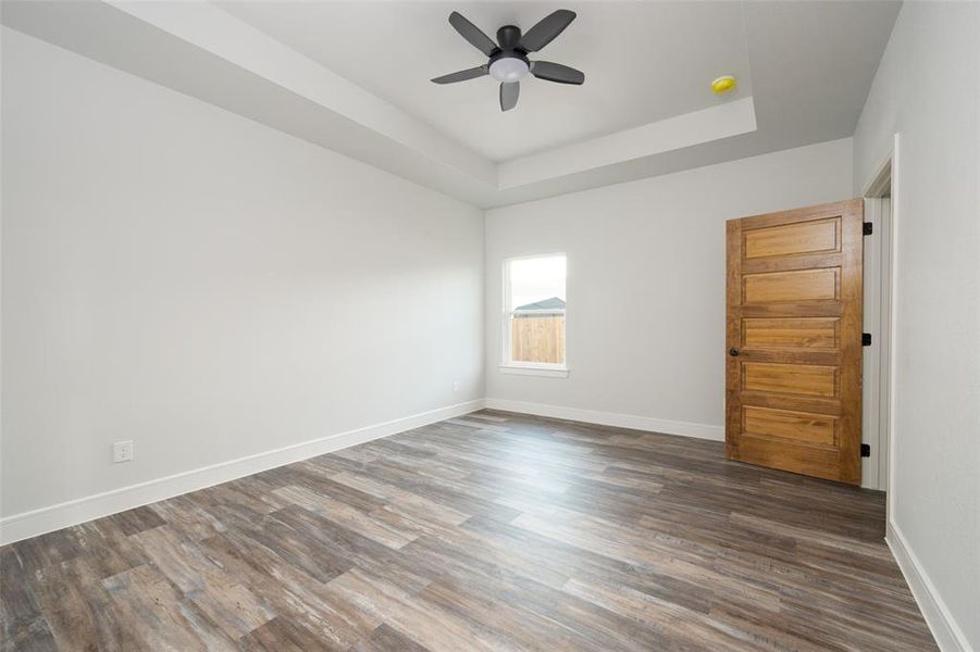 Empty room featuring a raised ceiling, dark wood finished floors, and a ceiling fan
