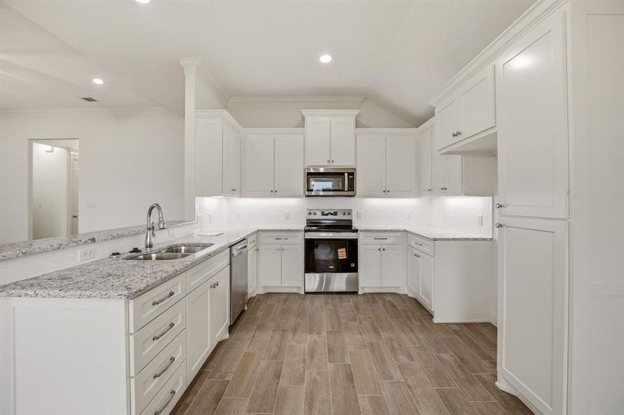 The kitchen features white cabinetry, speckled countertops, a double basin sink, and stainless steel appliances