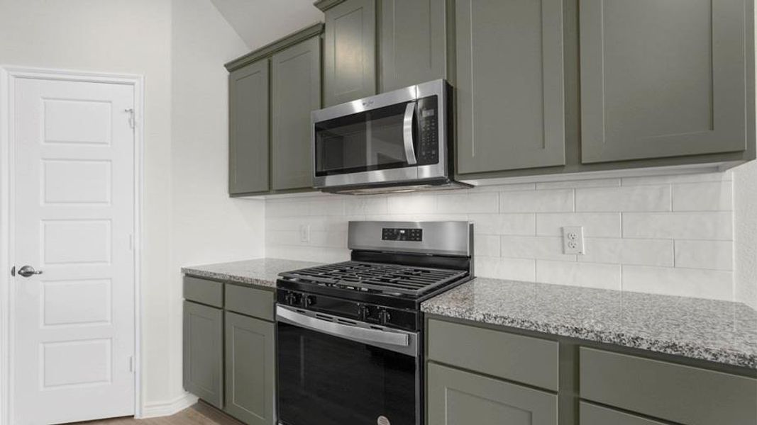 Kitchen featuring gray shaker-style cabinetry, a stainless steel gas range, a coordinating stainless steel microwave, a white subway tile backsplash, and speckled countertops