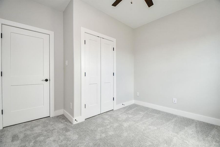 This is a bright great size,secondary bedroom featuring clean walls, plush carpeting, a ceiling fan, and built-in closet space with modern doors.