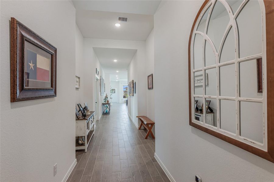 Elegant hallway with warm wood-look tile flooring, high ceilings, leading to an inviting open living space.