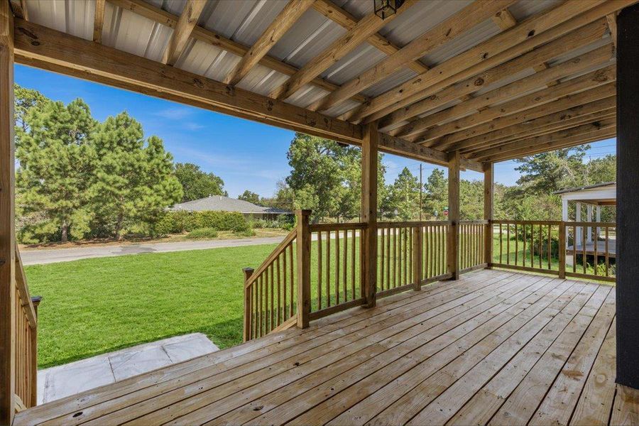 An elevated wood porch with a covered ceiling overlooks a spacious grassy yard. An elevated wood porch with a covered ceiling overlooks a spacious grassy yard.