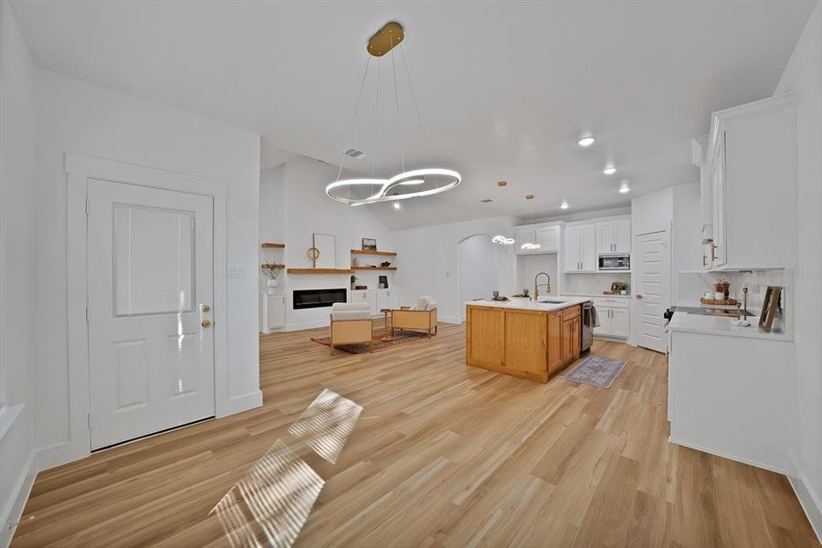 Kitchen with open floor plan, hanging light fixtures, a glass covered fireplace, white cabinetry, and lofted ceiling