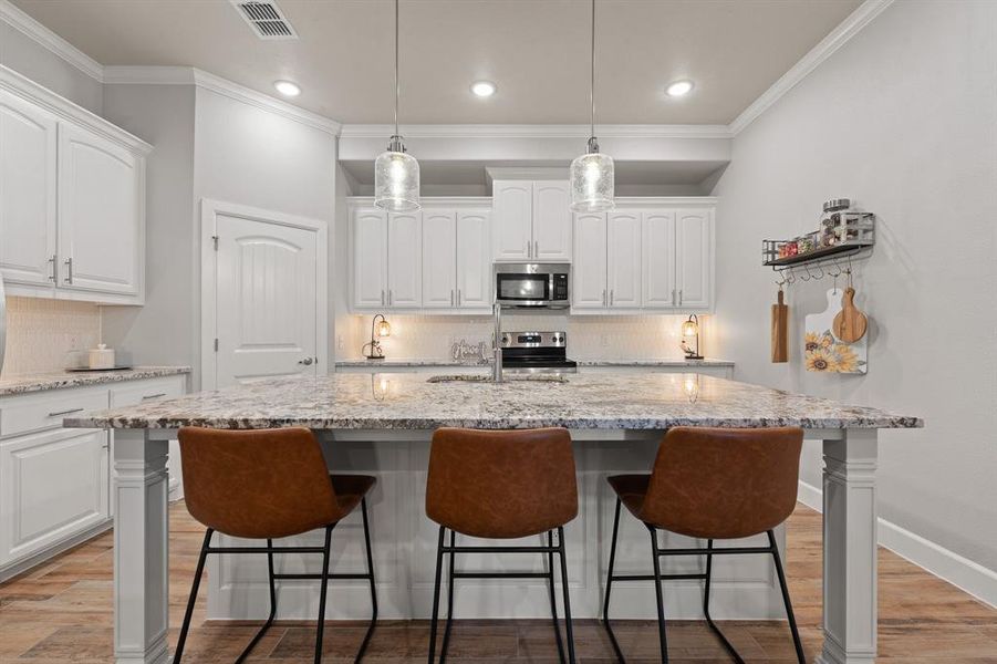 Kitchen with tasteful backsplash, white cabinets, light stone counters, crown molding, and recessed lighting