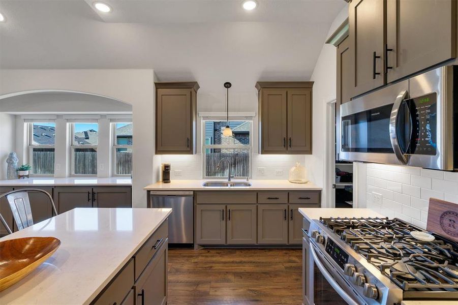 Kitchen featuring sink, hanging light fixtures, dark hardwood / wood-style floors, decorative backsplash, and appliances with stainless steel finishes