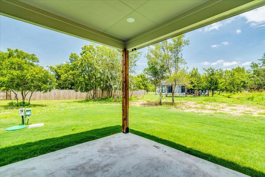 View from back patio, showcases a spacious yard with mature trees and a fenced perimeter. Offering a private, verdant retreat.
