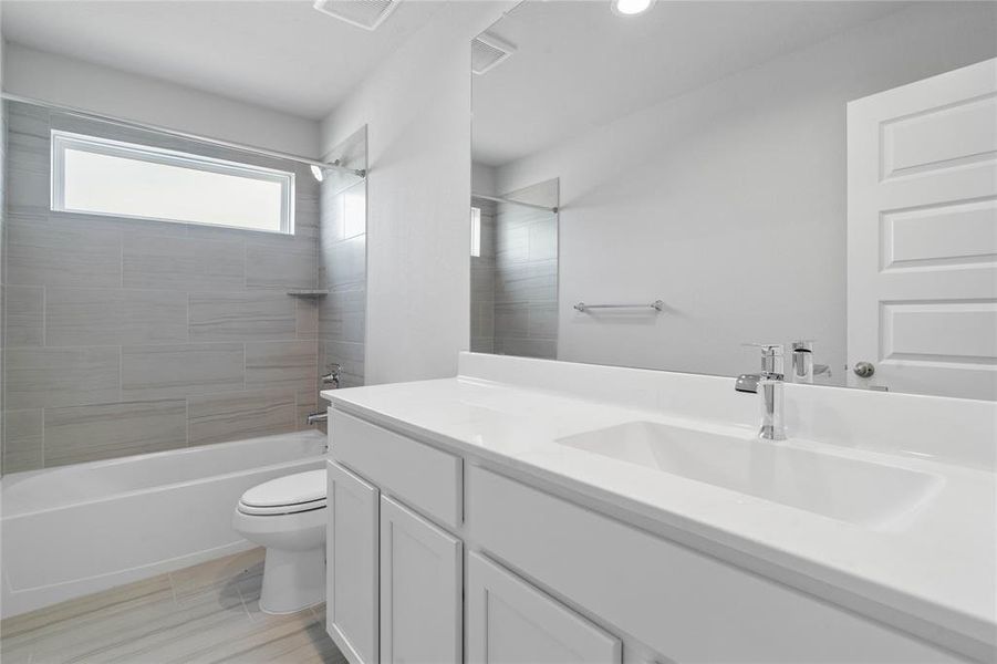 Secondary bath features tile flooring, tub/shower combo with tile surround, stained wood cabinets, beautiful light countertops, mirror, sleek fixtures and modern finishes.