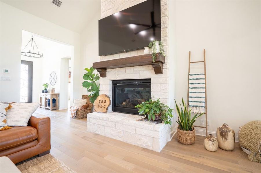 Living room with light wood-style floors, a stone fireplace, lofted ceiling, and hanging lights Living room with light wood-style floors, a stone fireplace, lofted ceiling, and hanging lights