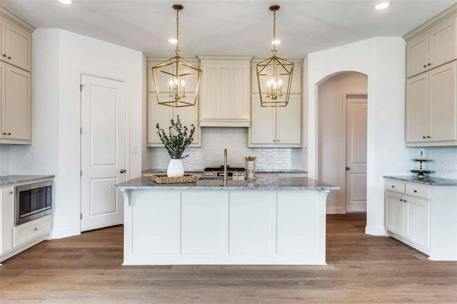 Kitchen with light stone countertops, decorative backsplash, decorative light fixtures, a kitchen island with sink, and recessed lighting