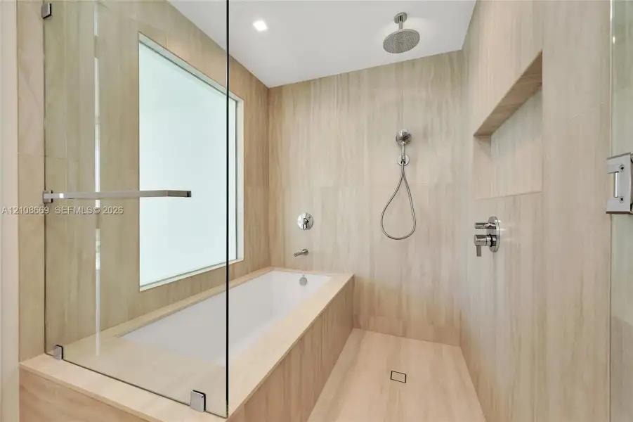 Wet room featuring a built-in soaking tub, large-format tile surround, frameless glass enclosure, ceiling-mounted rainfall showerhead, and recessed wall niche