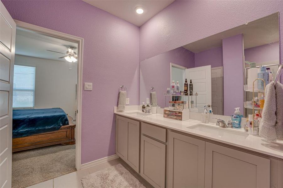 Bathroom featuring a textured wall, ensuite bathroom, double vanity, light tile patterned floors, and light colored carpet