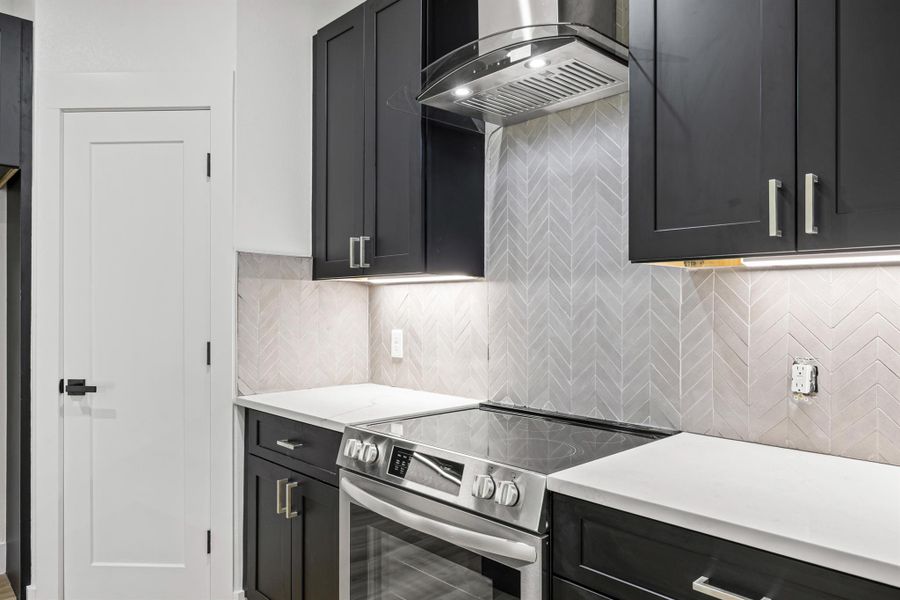 Kitchen featuring dark cabinets, electric stove, backsplash, wall chimney exhaust hood, and light stone countertops