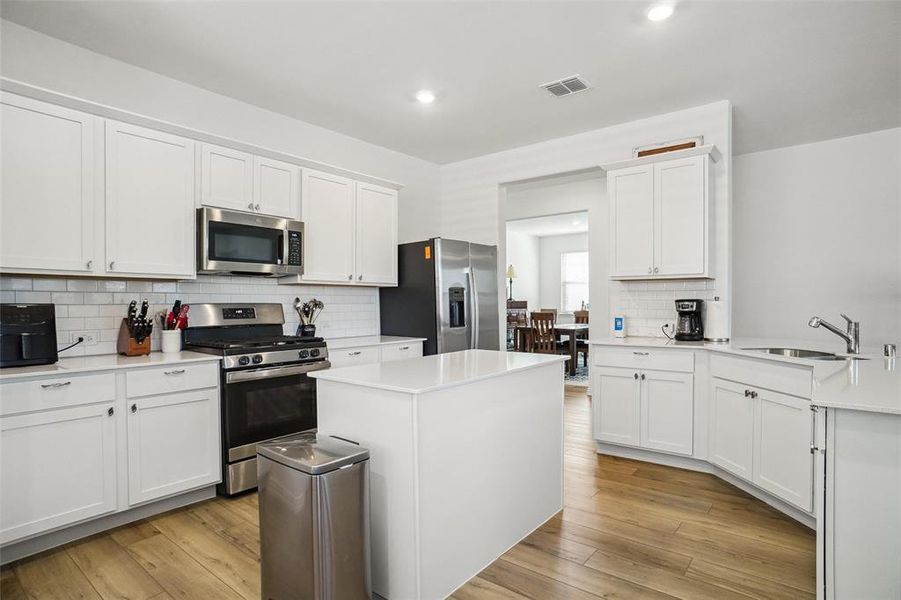 Kitchen with a center island, backsplash, sink, appliances with stainless steel finishes, and white cabinetry