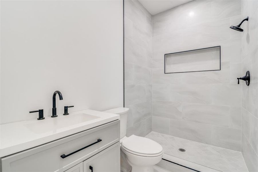 Bathroom with a tile shower, vanity, and toilet