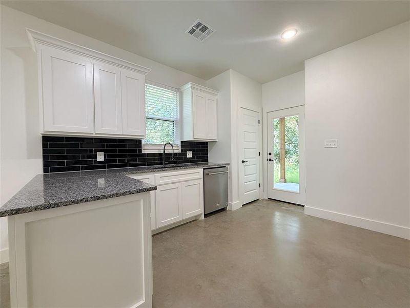 Kitchen featuring concrete flooring, backsplash, white cabinets, dark stone countertops, and stainless steel dishwasher