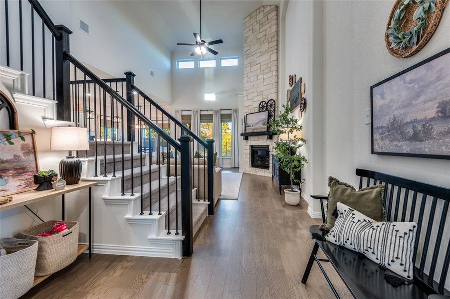 Stairway with wood finished floors, a stone fireplace, ceiling fan, and a high ceiling