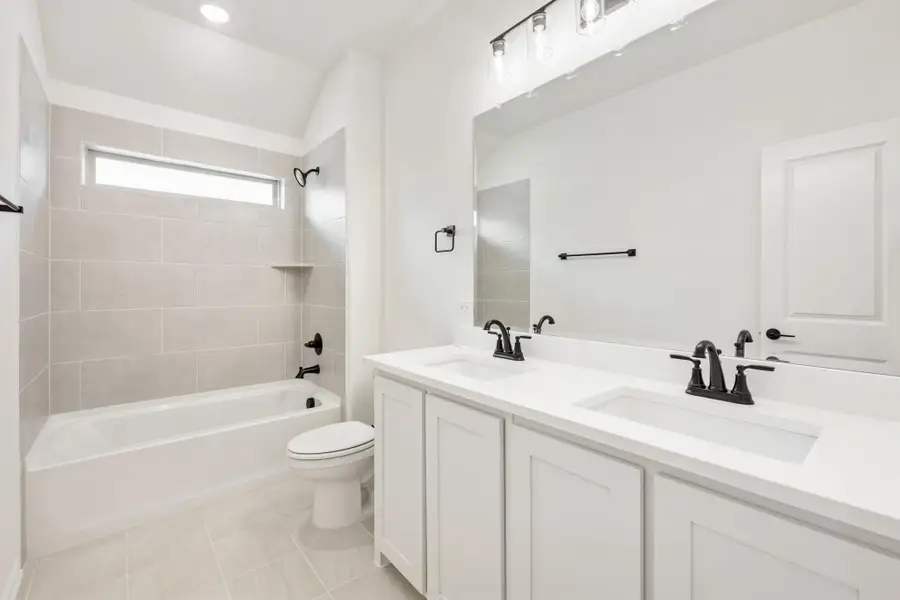 Bathroom with double sink vanity, white cabinets, tiled tub-shower combo, and black fixtures
