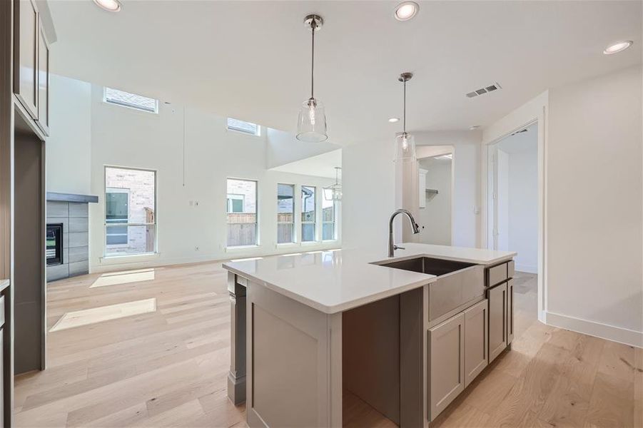 Kitchen with sink, light hardwood / wood-style flooring, decorative light fixtures, and an island with sink