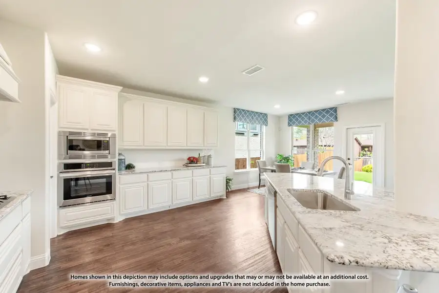 Kitchen with white cabinets, granite island, stainless steel double oven, and hardwood floors open to dining area.