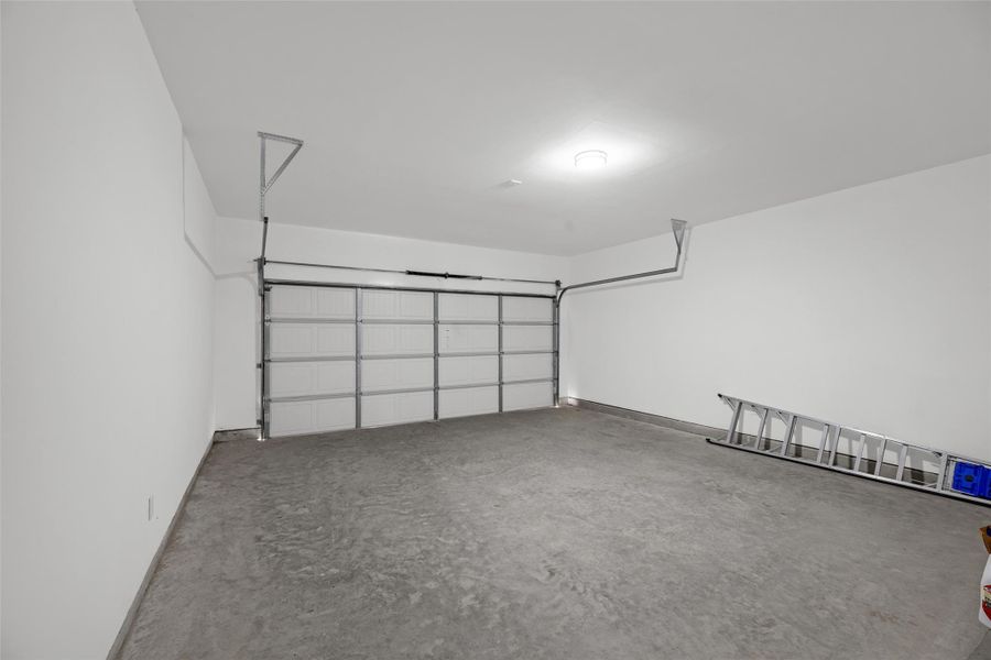 Clean garage with a concrete floor and a large, modern overhead door. The walls are white, and there's a ladder stored along one side, suggesting ample room for storage or projects.
