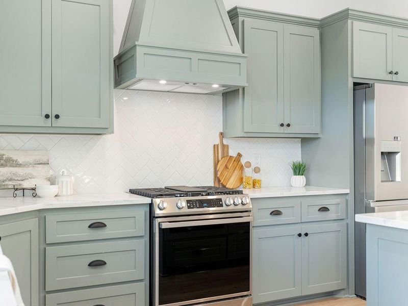 Kitchen with hanging light fixtures, stainless steel appliances, light wood-style flooring, light stone countertops, and backsplash