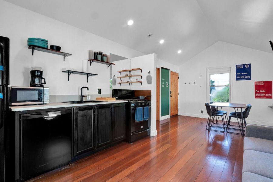 Kitchen with black appliances, open shelves, dark cabinetry, vaulted ceiling, and dark wood-type flooring