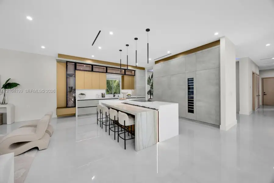 Custom kitchen featuring a stone-topped waterfall island, full-height cabinetry with integrated refrigeration, metallic-tone upper accent cabinets, and recessed ceiling lighting