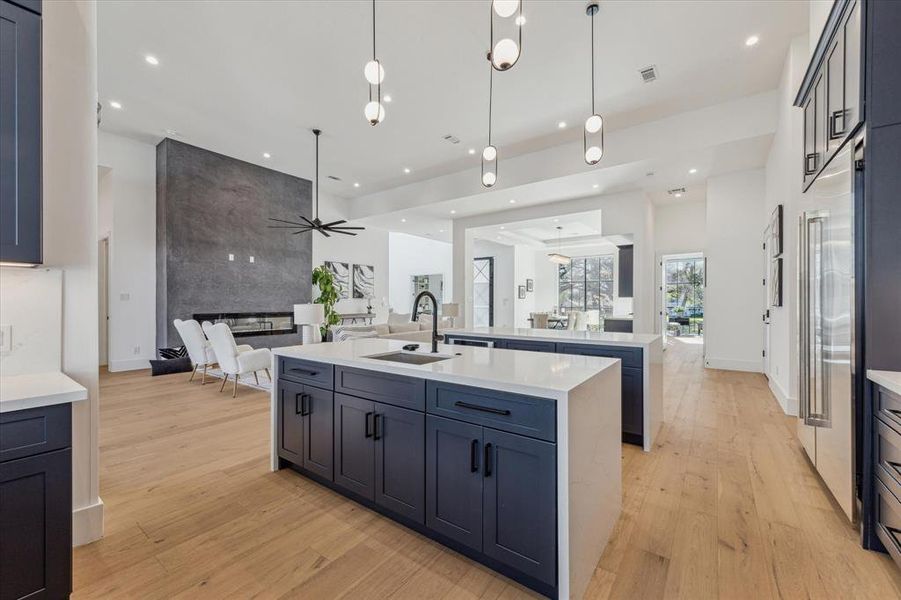 This kitchen features an open-concept layout with a large island seamlessly connecting to the family room, highlighted by a modern fireplace and high ceilings, enhancing the sense of space and flow.