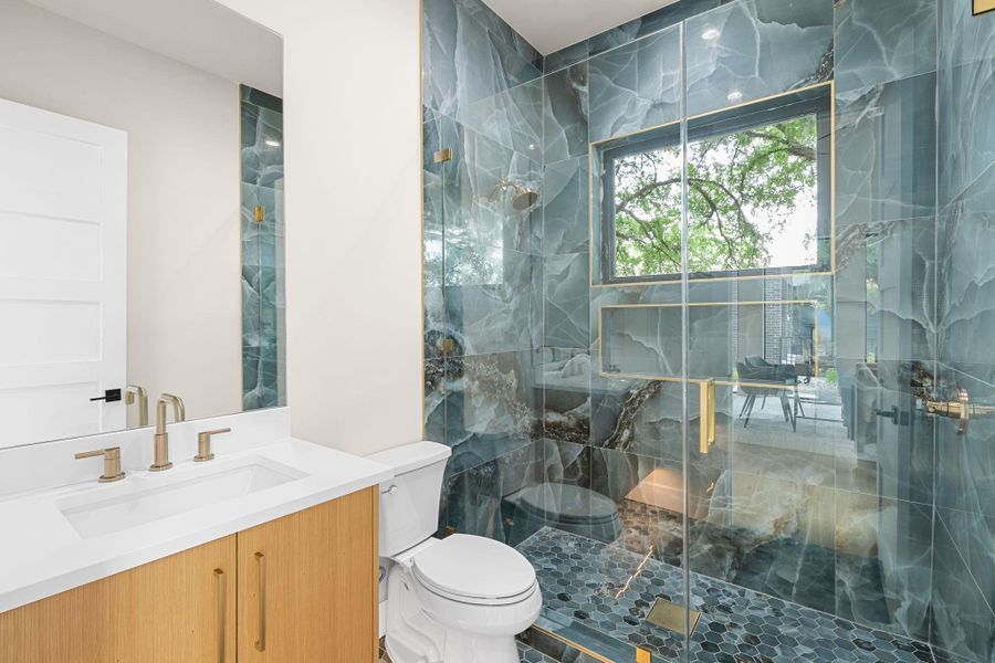 Contemporary bathroom featuring a spacious glass-enclosed shower with full-height tile surround, built-in shelving, and a brass-framed window
