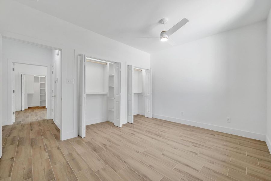 Unfurnished bedroom with wood finish floors, multiple closets, and a ceiling fan Unfurnished bedroom with wood finish floors, multiple closets, and a ceiling fan