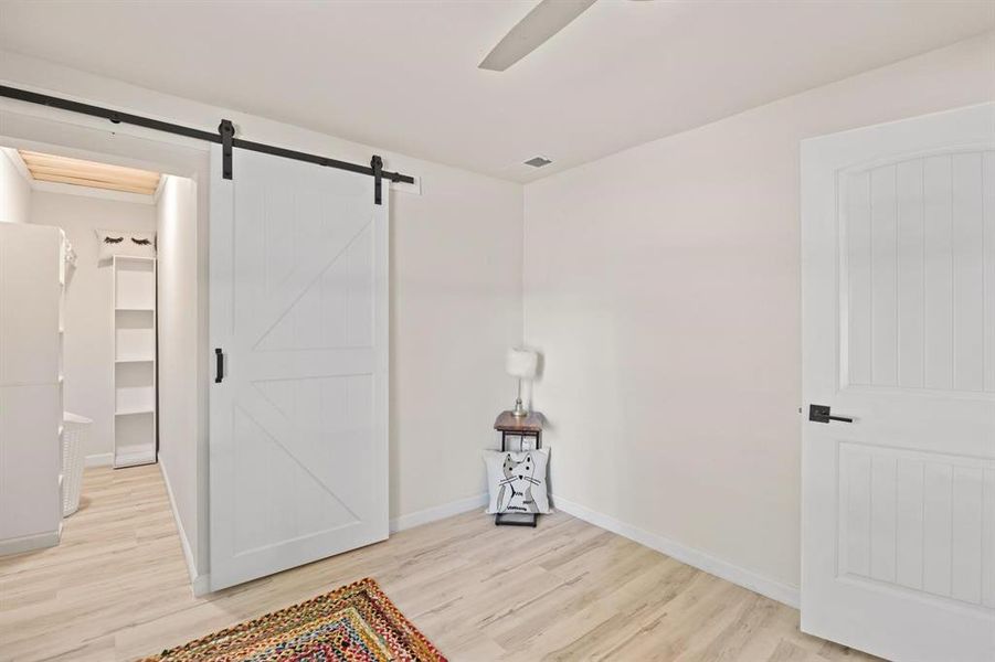 Bedroom with a barn door, ceiling fan, and light hardwood / wood-style flooring