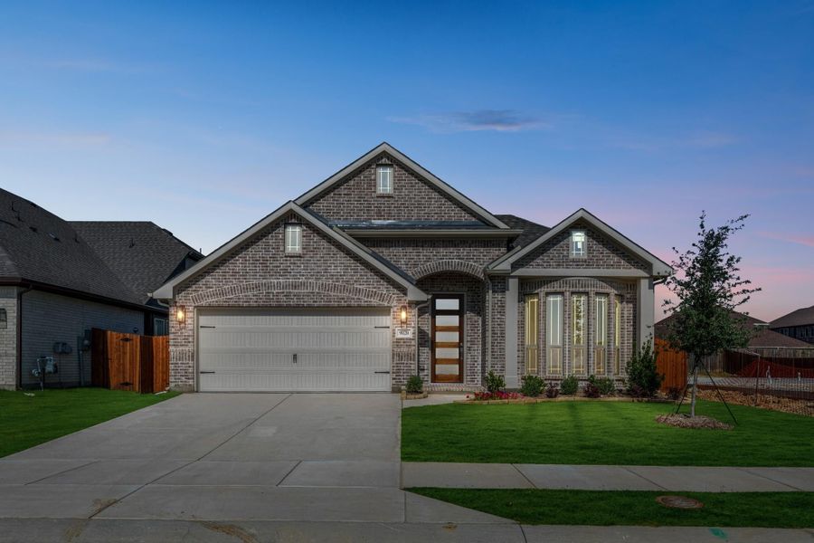 Single-story brick home with two-car garage, arched entry, and manicured lawn at dusk