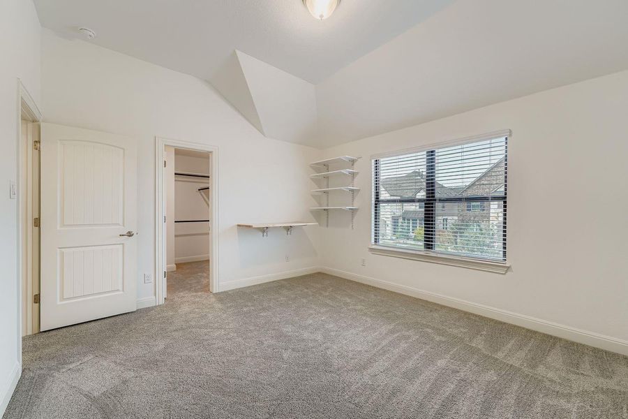 Unfurnished bedroom with a walk in closet, lofted ceiling, and light carpet Unfurnished bedroom with a walk in closet, lofted ceiling, and light carpet