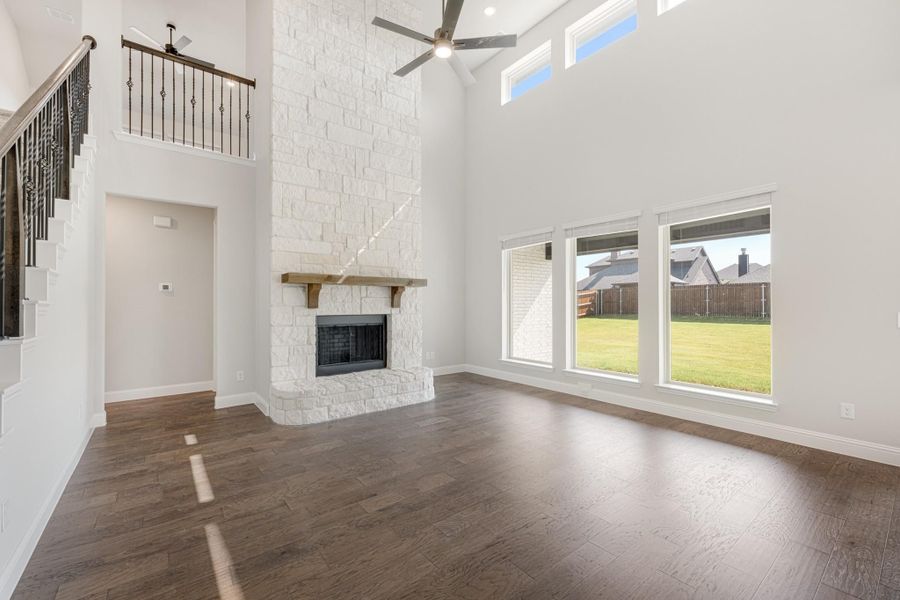 Open living room with two-story stone fireplace, dark hardwood floors, and ceiling fan Open living room with two-story stone fireplace, dark hardwood floors, and ceiling fan