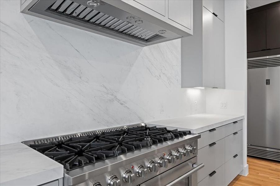 Kitchen with chef range, appliances with stainless steel finishes, light wood-type flooring, modern cabinets, and decorative backsplash Kitchen with chef range, appliances with stainless steel finishes, light wood-type flooring, modern cabinets, and decorative backsplash