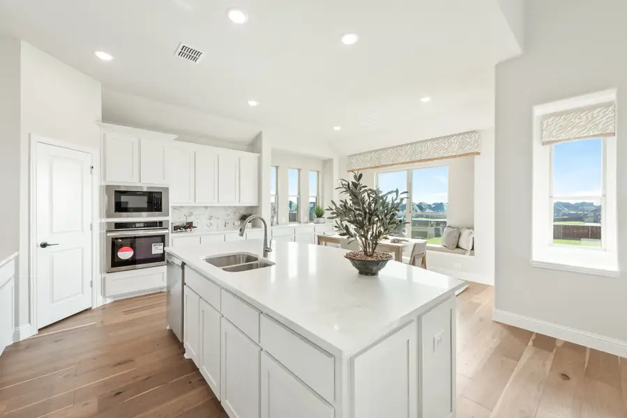 Kitchen with white cabinets, large island with sink, stainless steel appliances, and hardwood floors open to dining area.