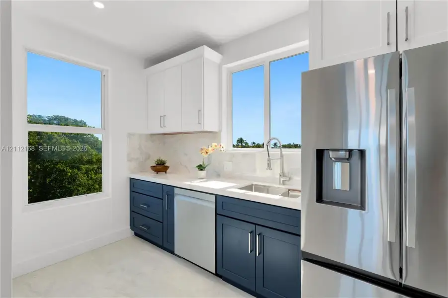 Kitchen featuring two-tone cabinetry, stone-finish countertops, stainless steel appliances, and large windows Kitchen featuring two-tone cabinetry, stone-finish countertops, stainless steel appliances, and large windows