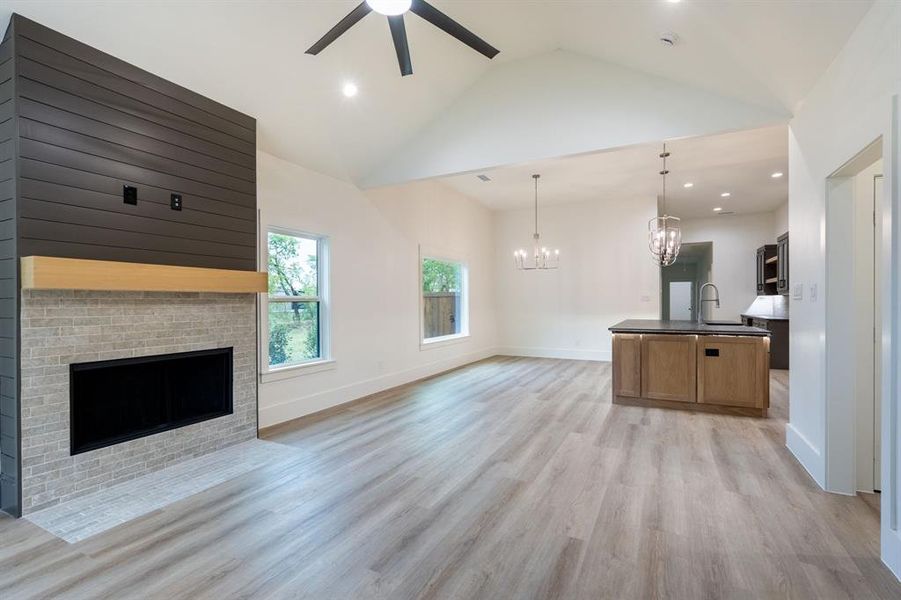 Unfurnished living room featuring a fireplace, light wood-type flooring, high vaulted ceiling, sink, and ceiling fan with notable chandelier