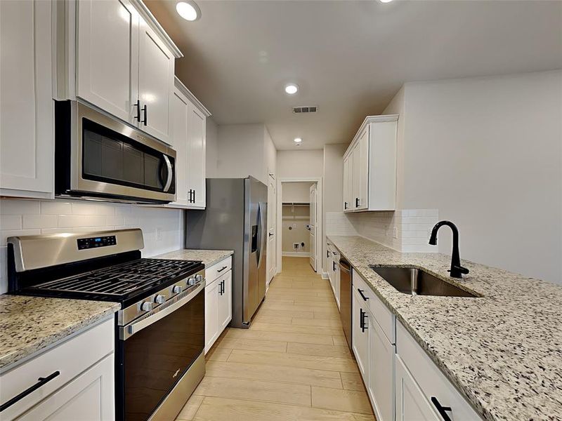 Kitchen with stainless steel appliances, sink, and white cabinets