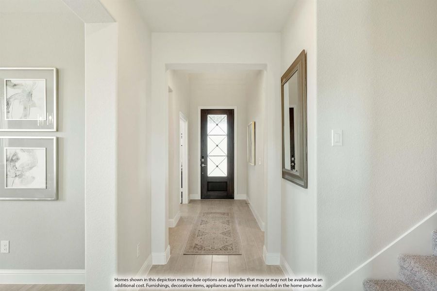 Bright entryway hallway with dark front door, glass panels, light wood floors, and wall art