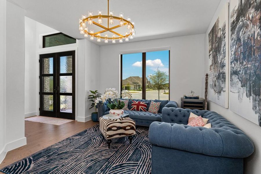 A well-lit living area features hardwood flooring, a unique chandelier, and a view of the neighborhood through a large window. A well-lit living area features hardwood flooring, a unique chandelier, and a view of the neighborhood through a large window.