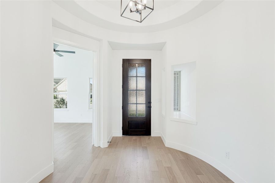 Bright home entryway with dark wood glass-panel front door, light hardwood floors, and modern chandelier.