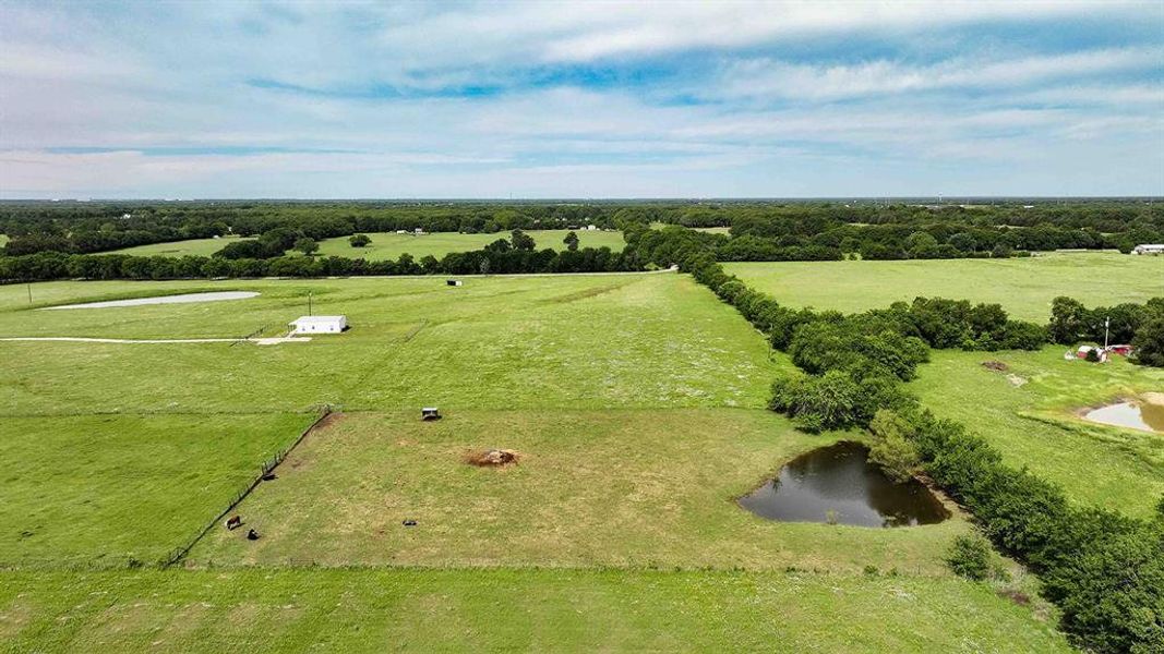 Expansive green acreage featuring a natural pond, scattered trees, and a distant white structure