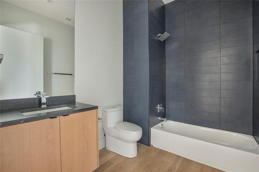 Full bathroom with wood-type flooring, toilet, vanity, and tiled shower / bath combo