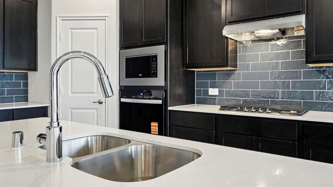 Kitchen featuring decorative backsplash, light stone counters, stainless steel appliances, and dark cabinetry